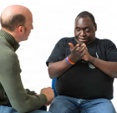 Two men engaged in a conversation, one listening intently while the other has his hands clasped.