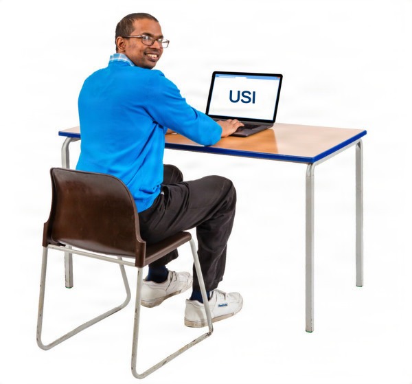 Man sitting at a table with a laptop showing 'USI', looking back and smiling.
