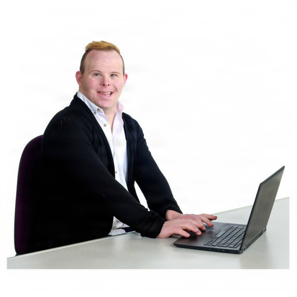 A person sitting at a desk, smiling, and working on a laptop.