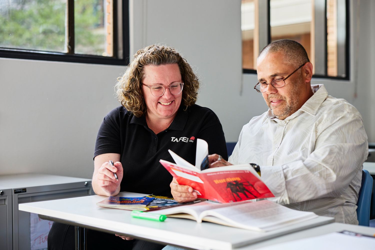 Two people reading a book together at a table.