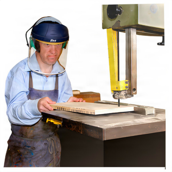 Man operating a band saw in a workshop while wearing protective gear.