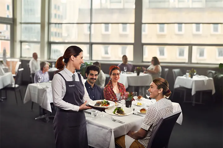 A server delivers food to smiling customers in a fine dining restaurant.