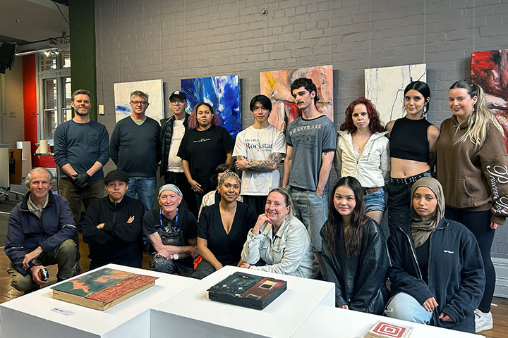 A group of students from the TAFE NSW Certificate IV in Arts and Cultural Administration (Galleries & Museums) facing the camera. A wall of contemporary artworks is behind them. 