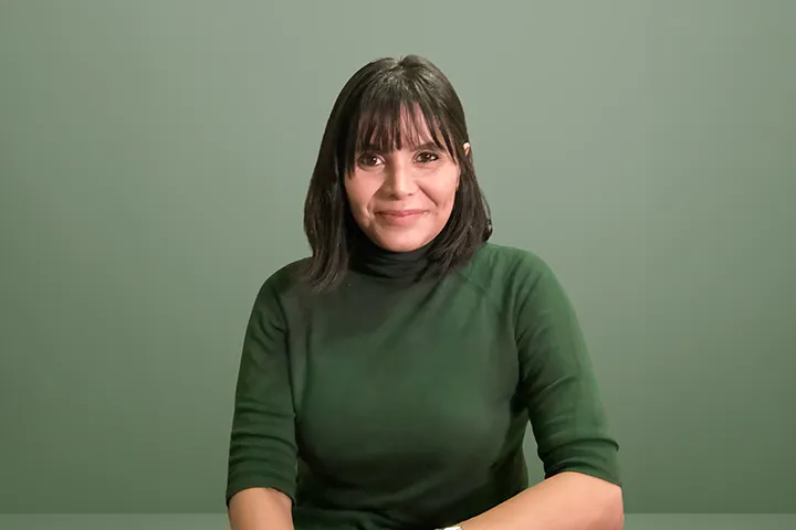 Patricia Lee, TAFE NSW Diploma graduate as well as Sustainability Projects & Strategy Manager at The University of Queensland smiles directly at the camera. She has dark, shoulder length hair with a fringe and wears a forest green, polar neck jumper. She appears seated. 