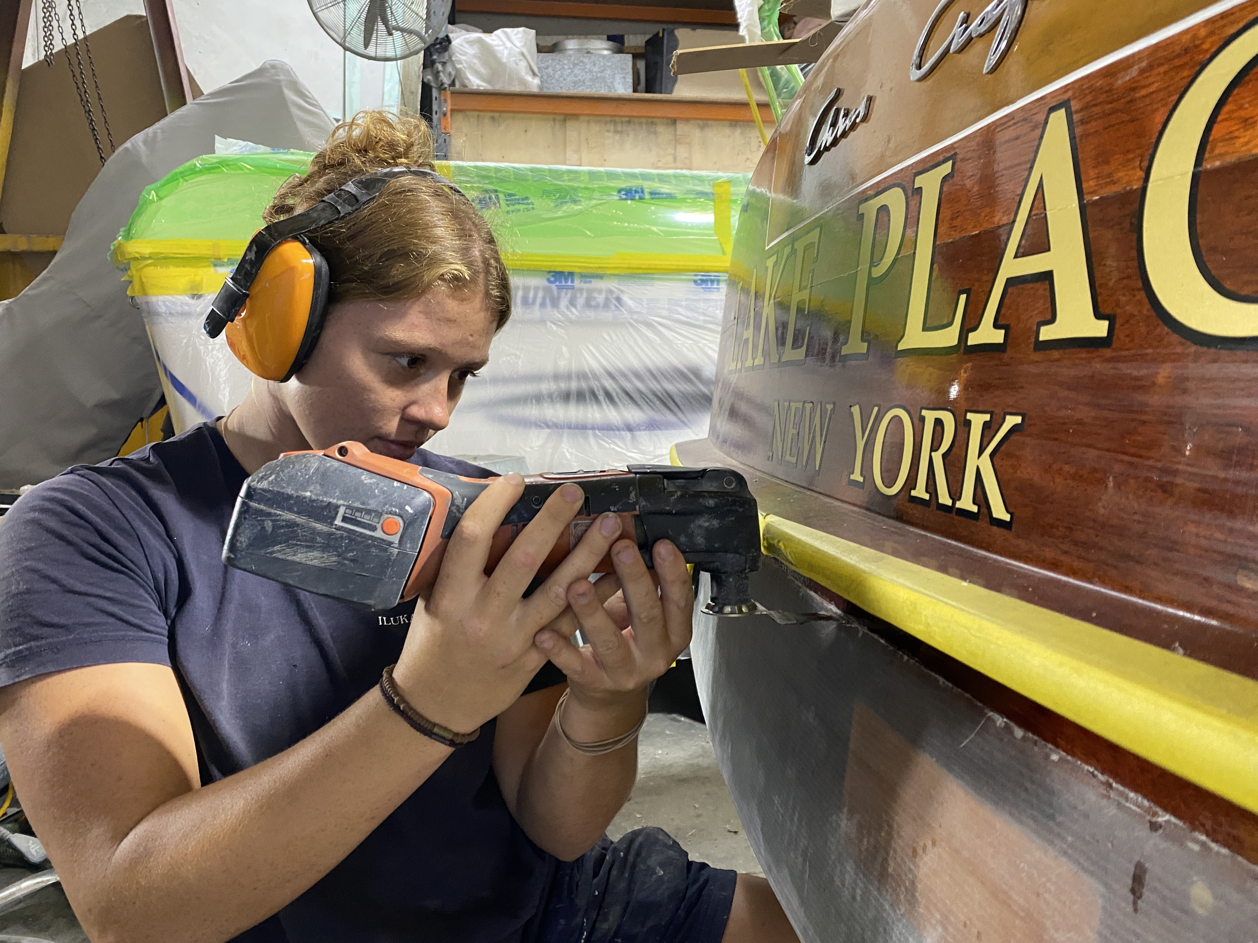 TAFE NSW graduate, Talia Dunning, wears protective earmuffs as she repairs a boat using a specialised hand tool.